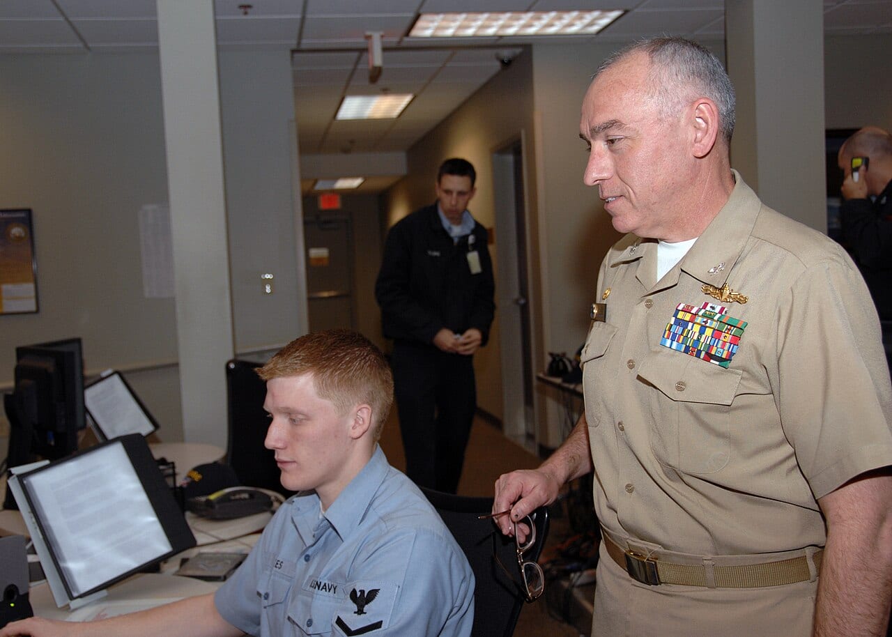 The commanding officer of Navy Cyber Defense Operations Command observing a watchstander at a monitoring console during a daily security shift.