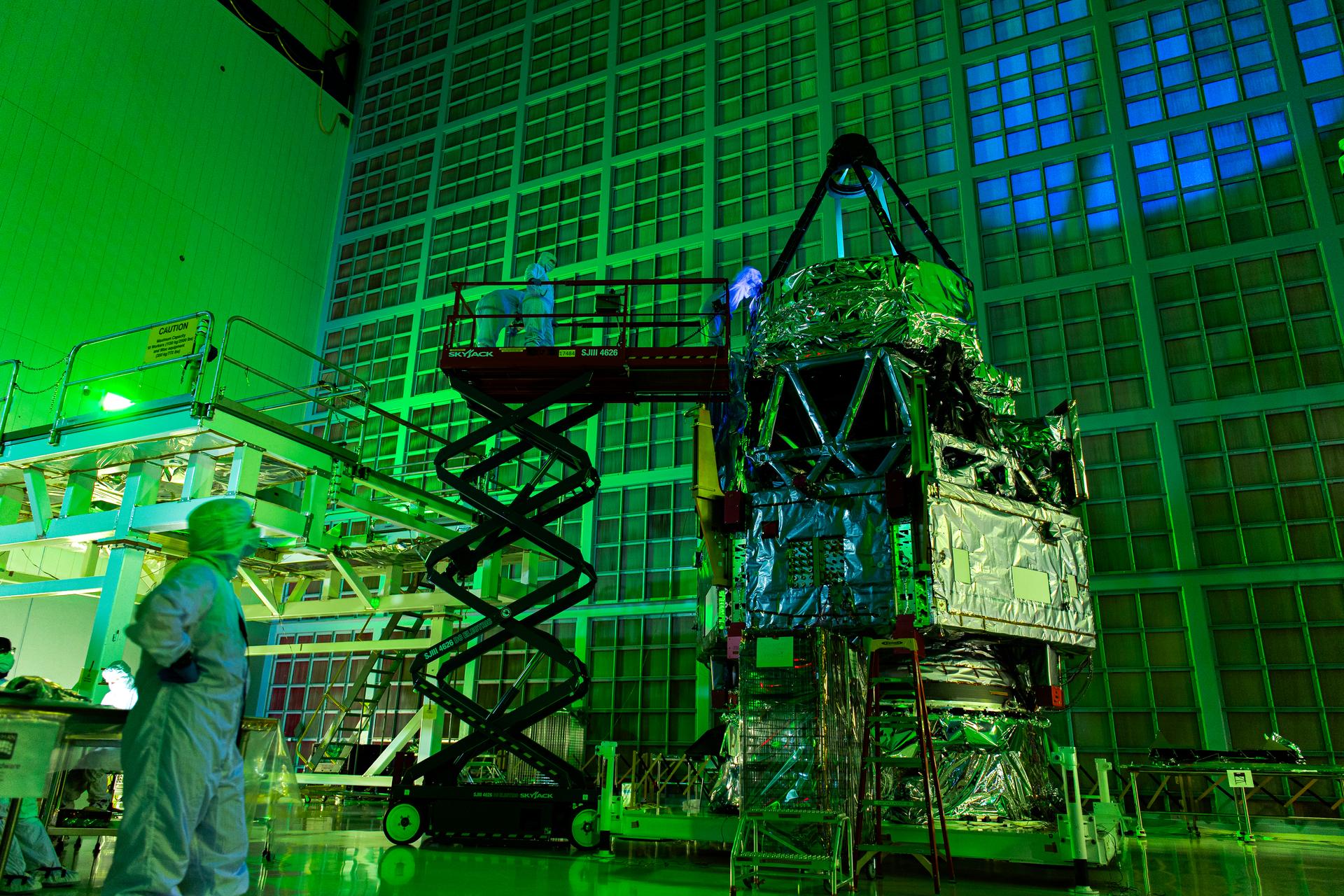 Roman Space Telescope team members inspecting the 2.4-metre primary mirror in the dark with flashlights and UV lights, checking for contamination in a Goddard Space Flight Center cleanroom.