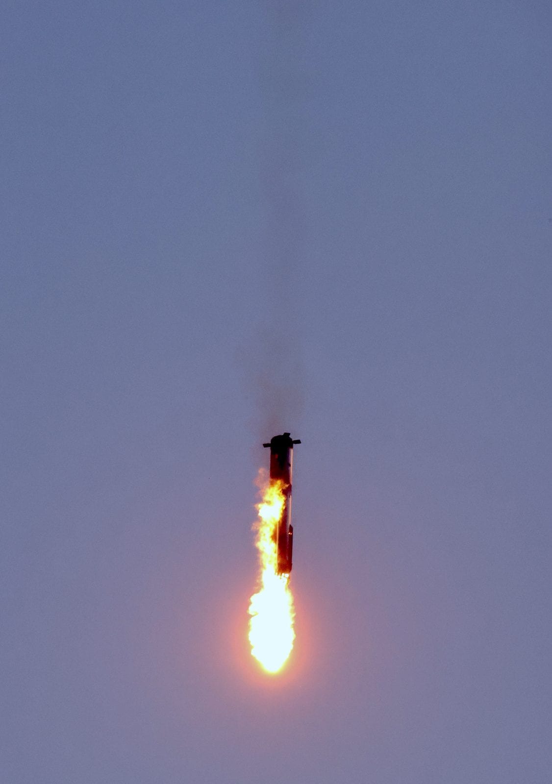 Super Heavy booster descending under power during its landing burn on the IFT-5 catch attempt, engine plume lit against the sky.